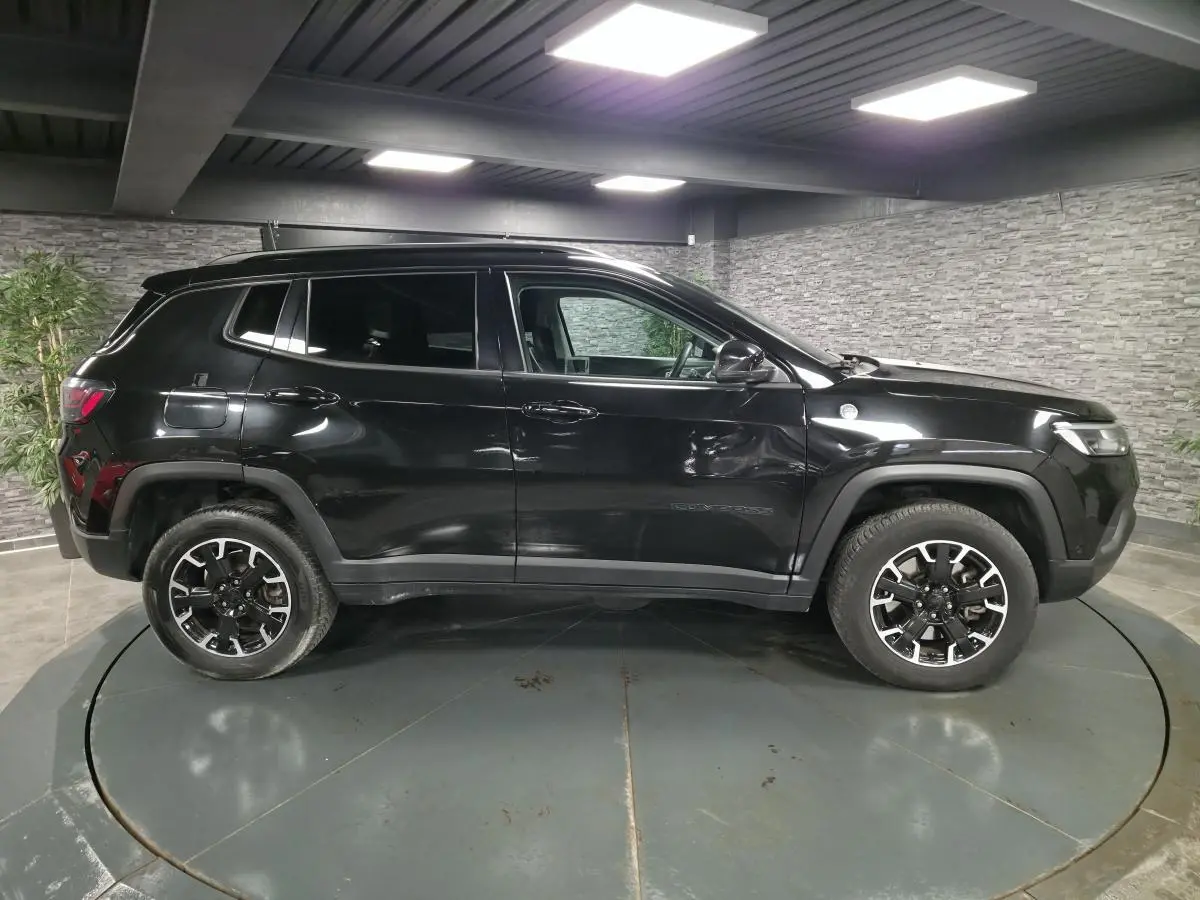 Vue latérale droite d'un Jeep Compass Trailhawk noir avec jantes alliage noires et vitres surteintées dans un showroom.