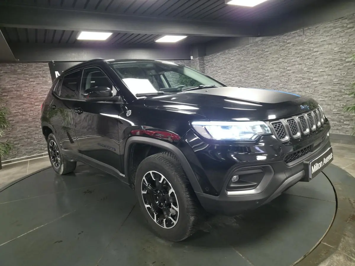 Jeep Compass Trailhawk noir vu en 3/4 avant droit avec phares allumés dans un showroom.