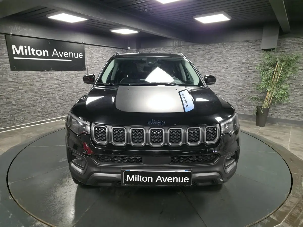 Vue avant d'un Jeep Compass Trailhawk noir avec sticker Trailhawk sur le capot, en intérieur showroom.