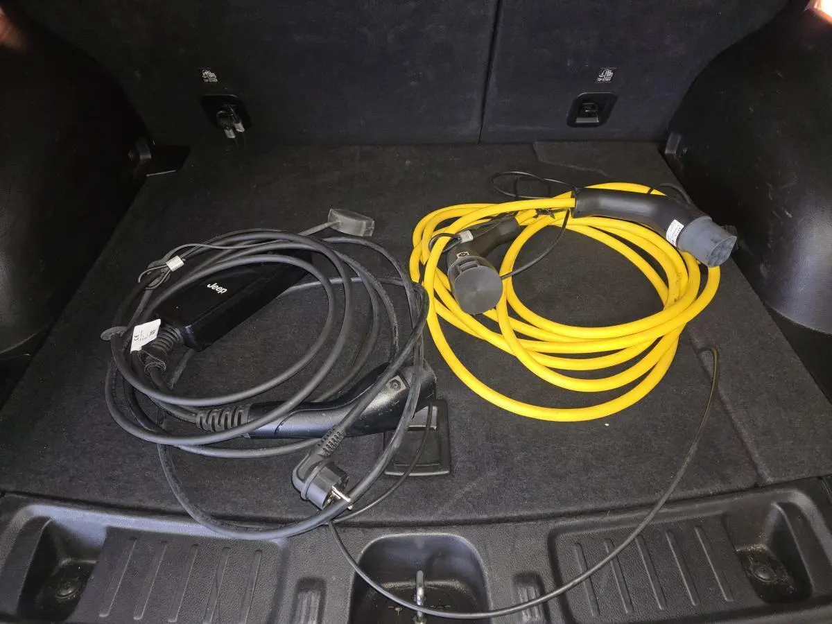 Coffre ouvert d’un Jeep Compass noir 2022 montrant deux câbles de recharge hybride, un noir et un jaune.