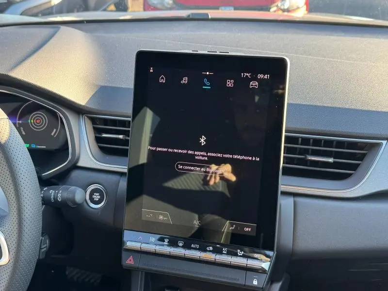 Vue intérieure centrée sur l'écran tactile vertical du tableau de bord du Renault Captur rouge 2025, avec volant partiel à gauche.
