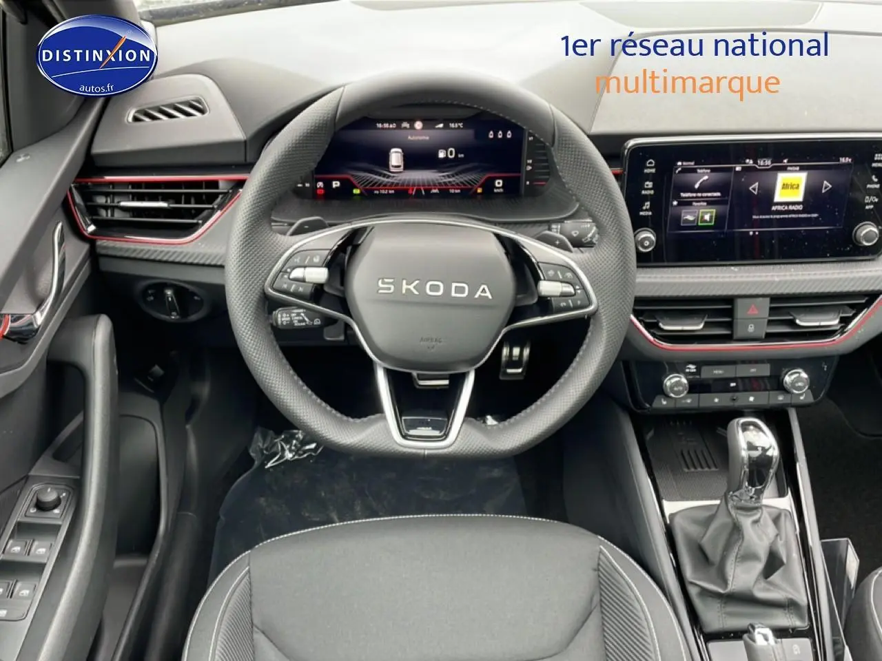 Vue intérieure centrée sur le volant SKODA noir et le tableau de bord avec écran tactile et détails rouges.