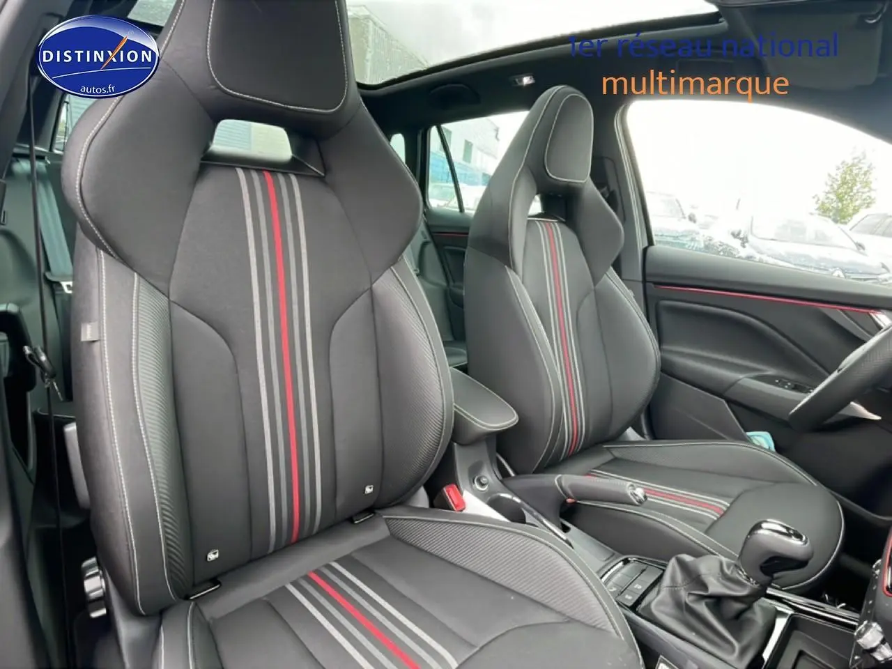 Vue intérieure en gros plan des sièges avant noirs avec bandes rouges et grises du Skoda Kamiq Monte Carlo 2026, toit panoramique visible.