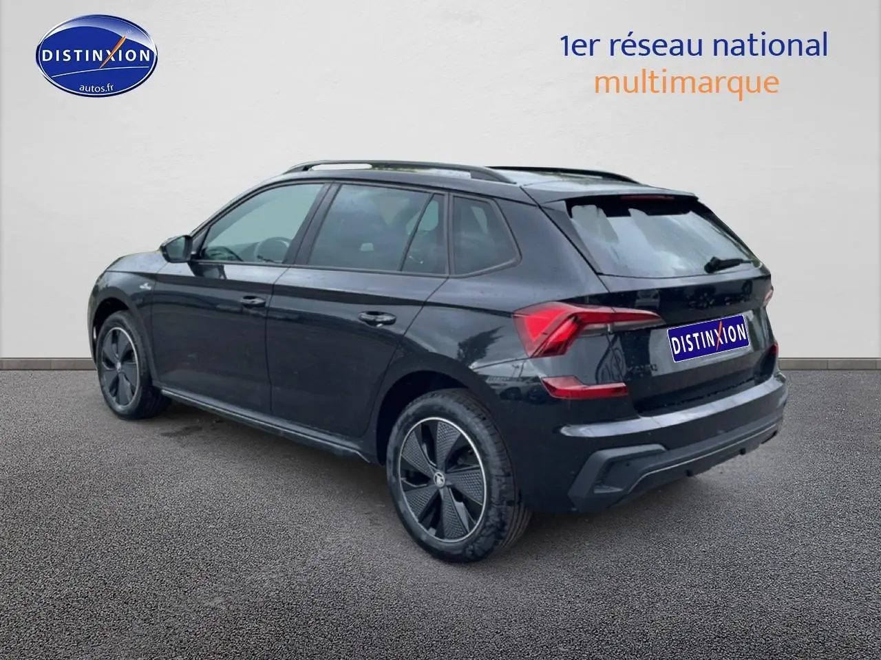 Vue 3/4 arrière droite d'un Skoda Kamiq noir avec jantes alu et barres de toit, sur fond neutre.
