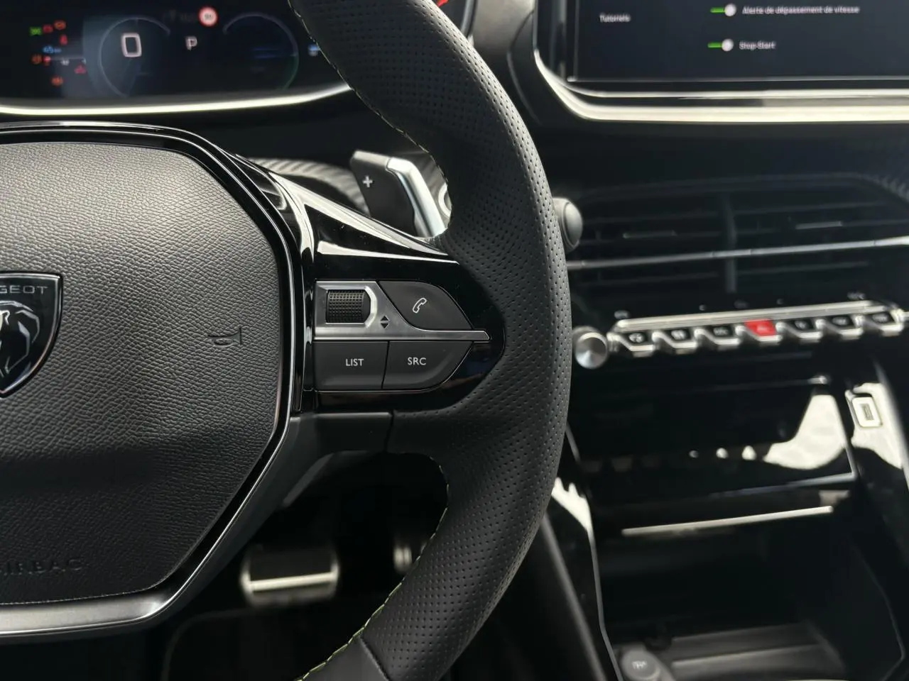 Gros plan sur le volant cuir perforé et la console centrale noire brillante du Peugeot 208 Hybrid 110 e-DSC6 GT.
