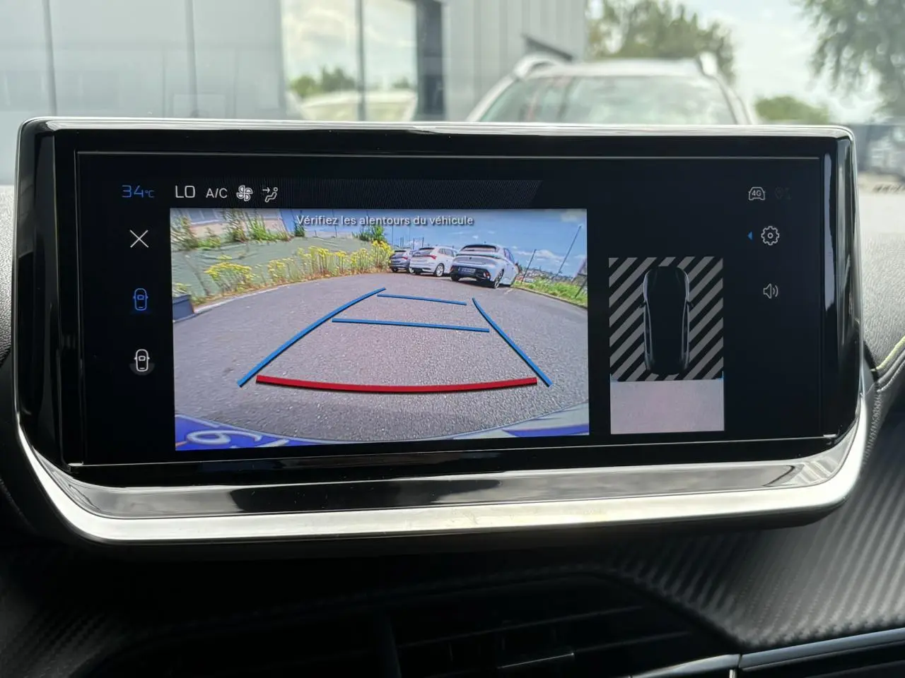 Écran tactile intérieur montrant la caméra de recul avec vue arrière et lignes de guidage sur Peugeot 208 Bleu Vertigo.