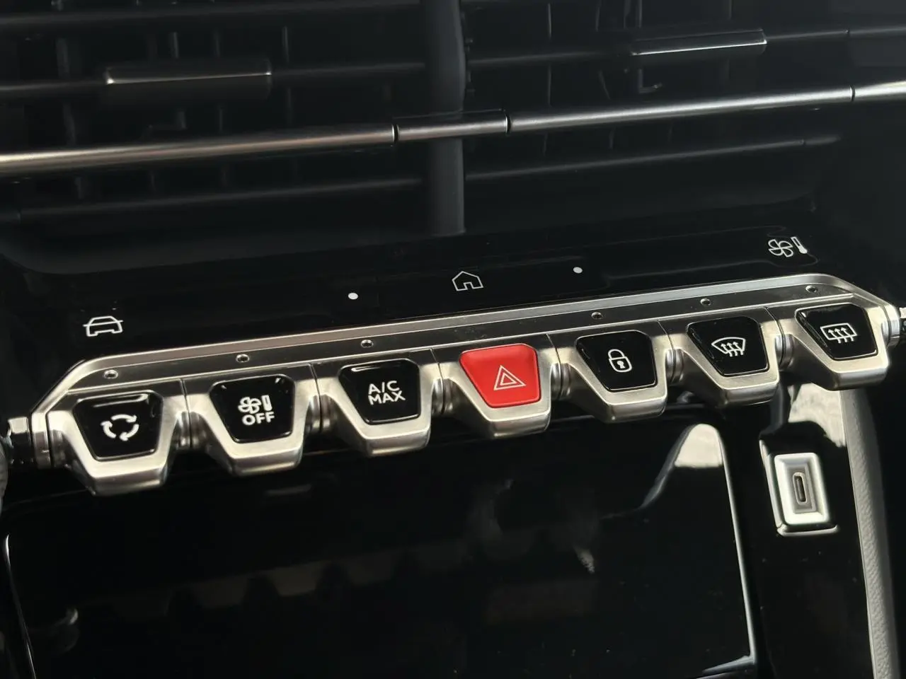 Gros plan sur la rangée de boutons de commande métalliques et noirs avec un bouton rouge au centre dans l’habitacle noir du Peugeot 208 Hybrid 110 GT.