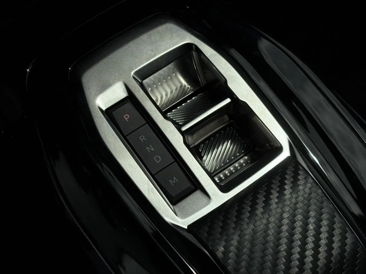 Gros plan sur la console centrale avec sélecteur de boîte automatique et finition carbone du Peugeot 208 Hybrid 110 GT.