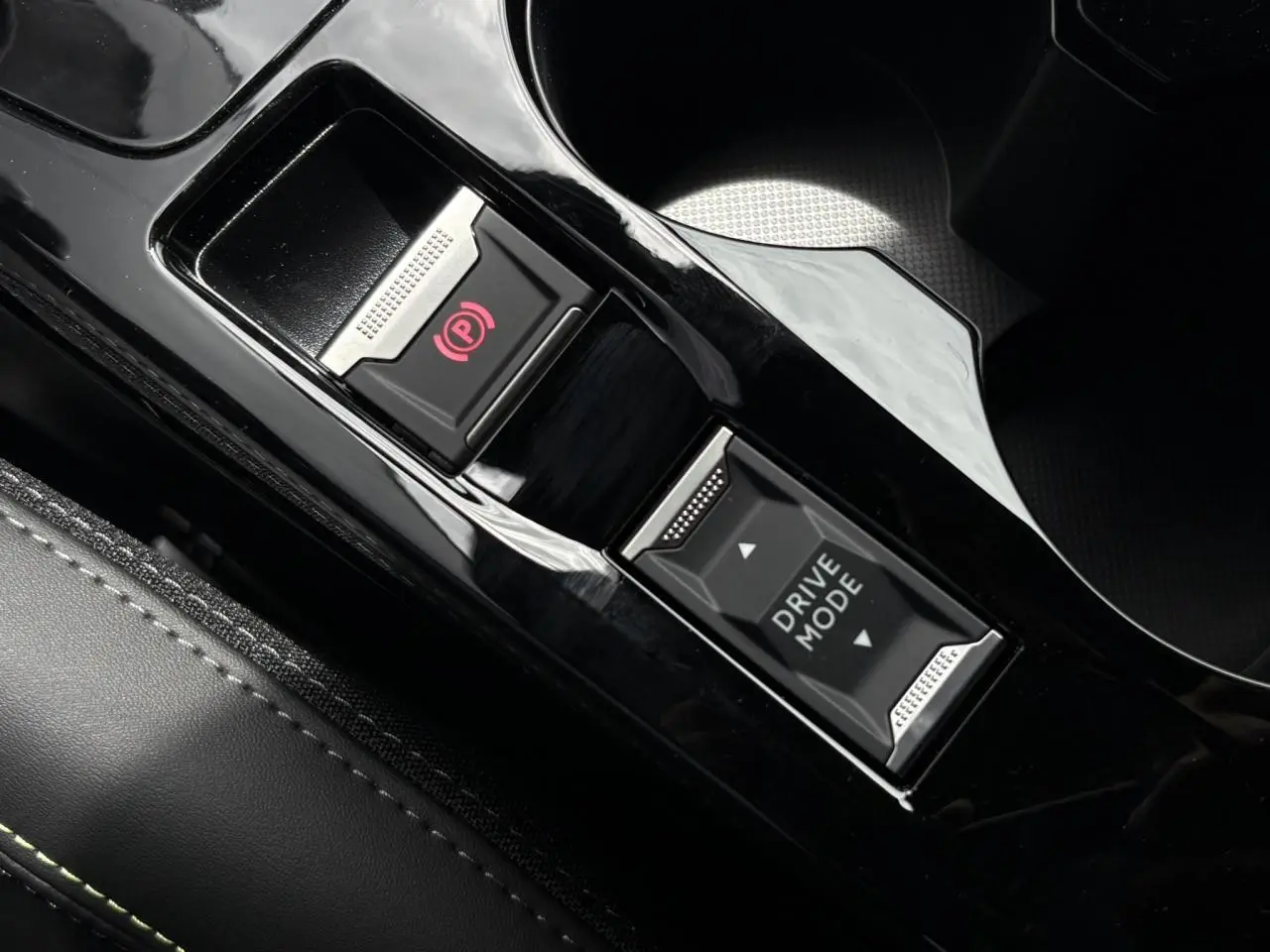 Gros plan sur la console centrale noire brillante de la Peugeot 208 Hybrid 110 e-DSC6 GT avec bouton frein électrique et sélecteur Drive Mode.