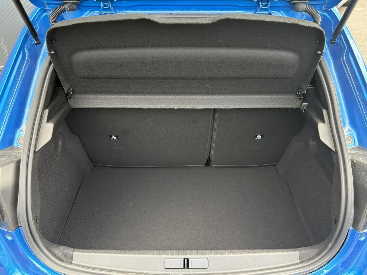 Coffre ouvert vu de l'arrière d'une Peugeot 208 Hybrid 110 e-DSC6 GT bleu Vertigo, montrant l'espace de chargement vide.