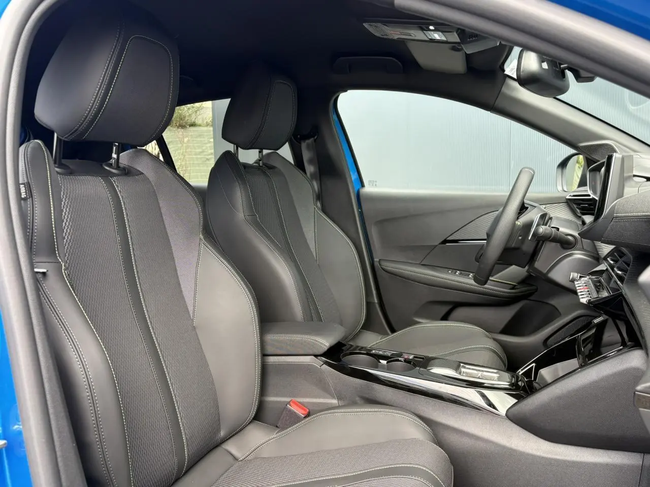 Intérieur avant droit de la Peugeot 208 Hybrid 110 GT bleu Vertigo, sièges tissu et TEP avec surpiqûres vertes.