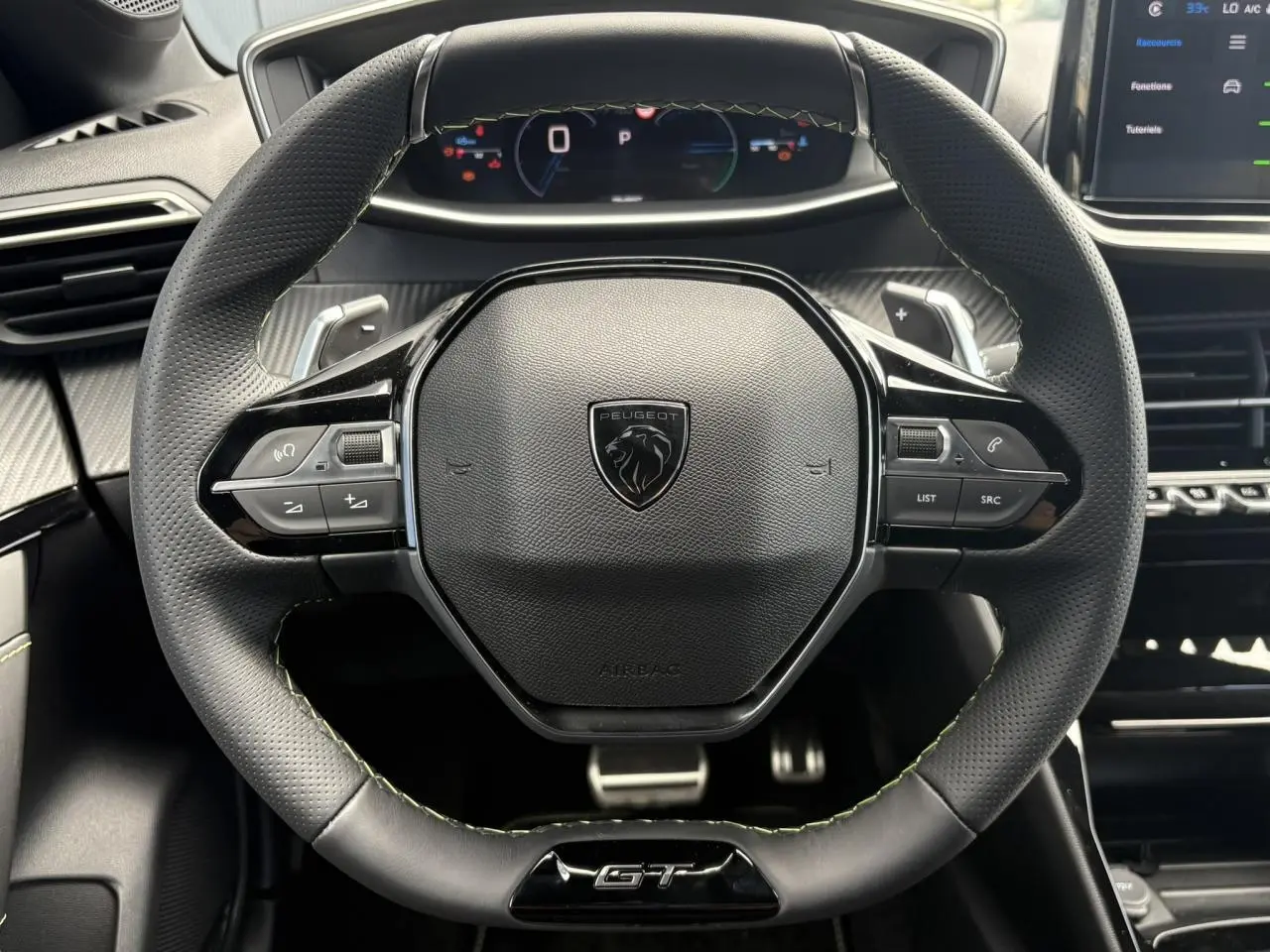 Volant cuir perforé Peugeot 208 Hybrid GT vu de face avec badge GT et commandes intégrées, intérieur noir et surpiqûres vertes.