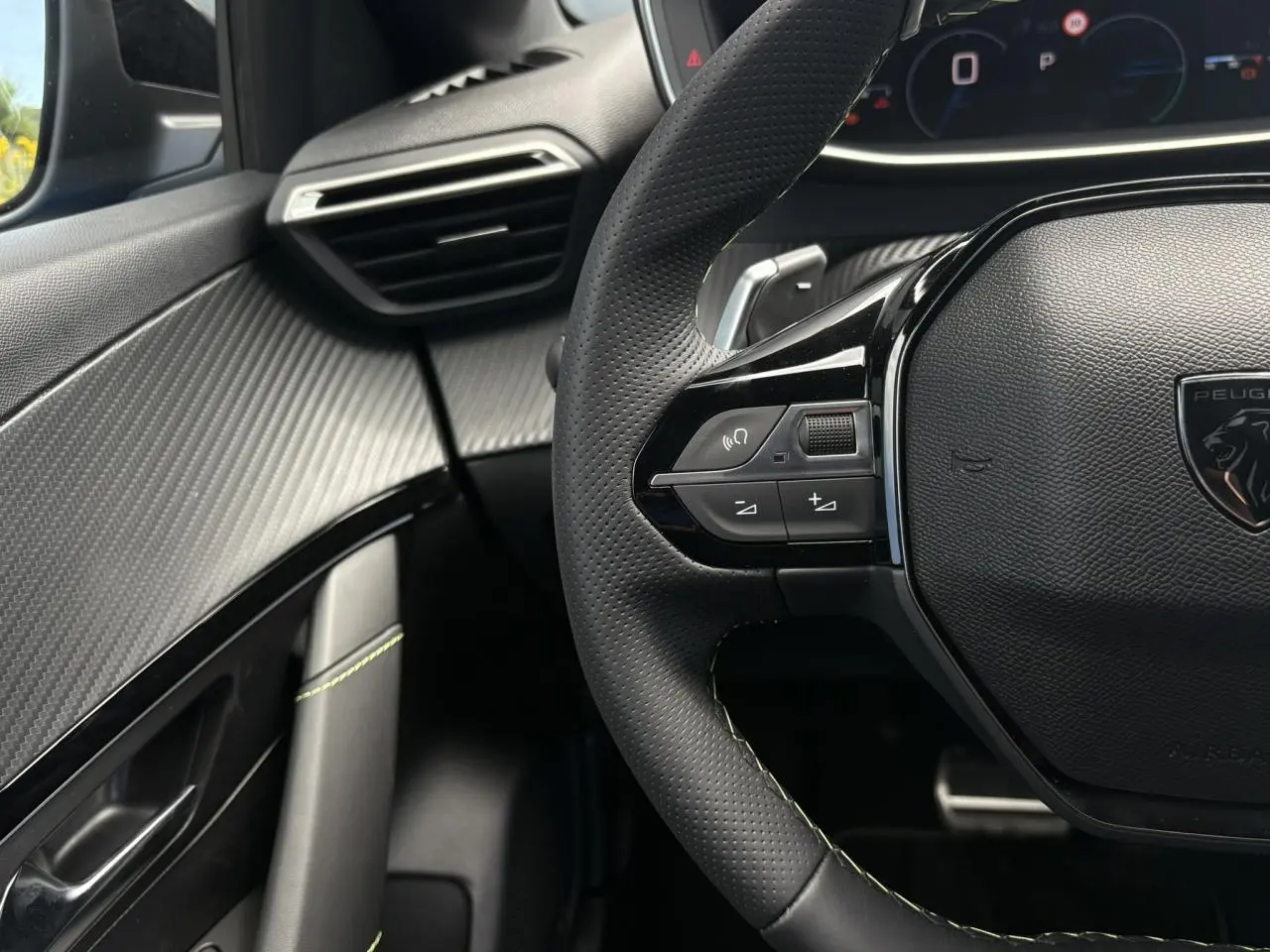 Vue rapprochée du volant cuir perforé avec commandes multimédia et tableau de bord numérique de la Peugeot 208 Hybrid GT.