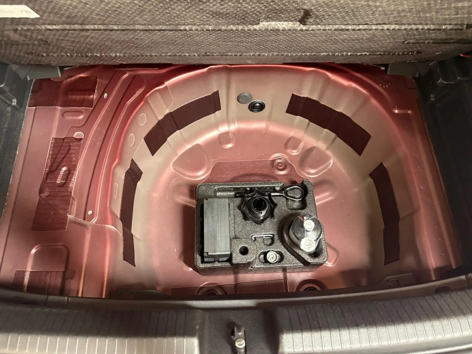 Vue plongeante sur le coffre ouvert d'une Volkswagen Polo Rouge Roi, montrant la zone de rangement sous le plancher sans roue de secours.