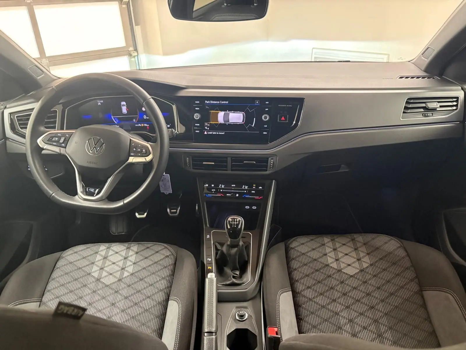 Vue intérieure avant du tableau de bord et volant Volkswagen Polo 2025 avec boîte manuelle et sièges tissu à motif géométrique.