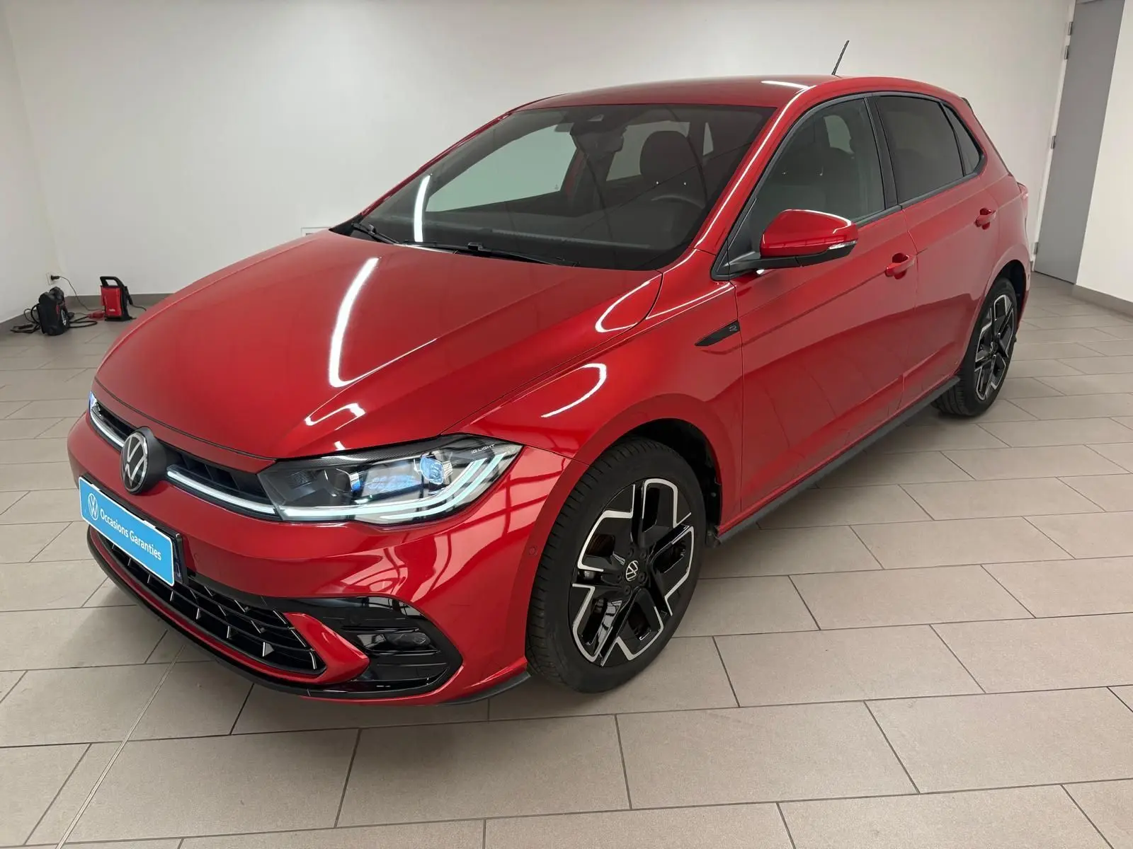 Volkswagen Polo 1.0 TSI R-Line rouge métallisé vue 3/4 avant droit en intérieur avec jantes noires distinctives.