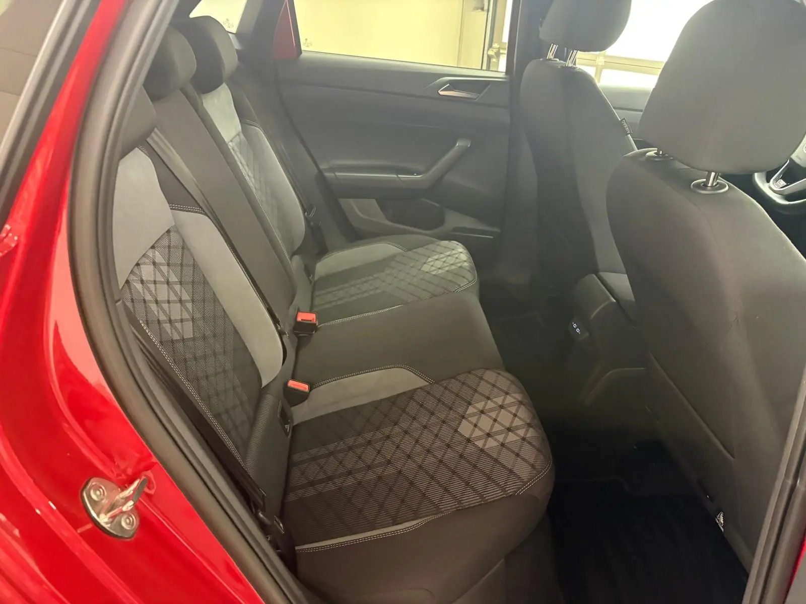 Vue intérieure arrière côté gauche d'une Volkswagen Polo Rouge Roi, sièges tissu avec motif géométrique et surpiqûres blanches.