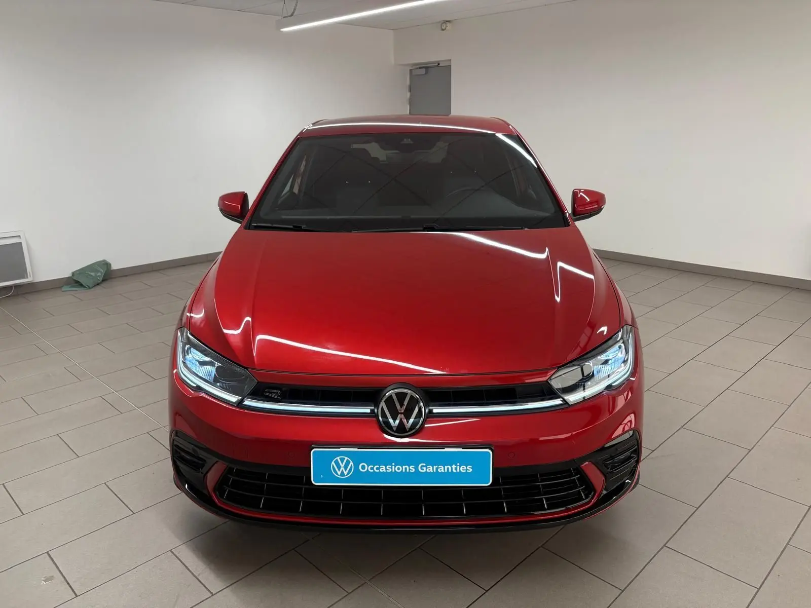 Vue frontale d'une Volkswagen Polo 1.0 TSI R-Line rouge métallisé, avec calandre noire et phares LED allumés.