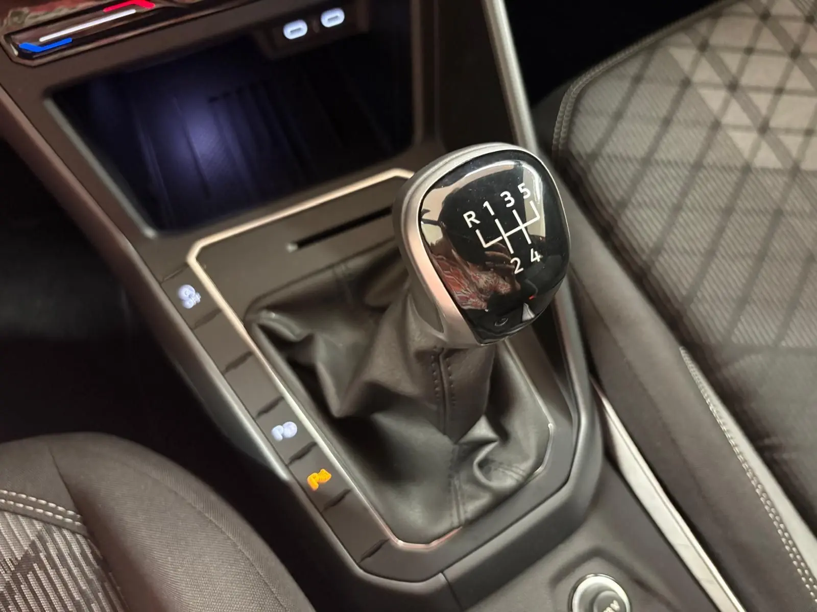 Gros plan sur le levier de vitesses manuel de la Volkswagen Polo 1.0 TSI R-Line, entouré de sièges tissu gris à surpiqûres blanches.
