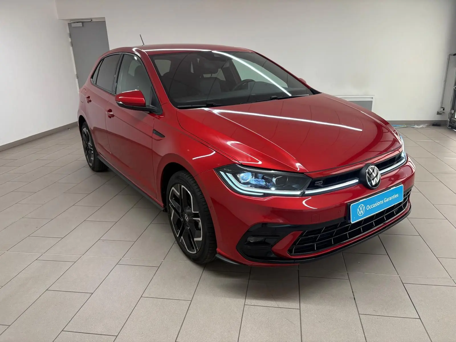 Volkswagen Polo 1.0 TSI R-Line rouge métallisé vue 3/4 avant droit en intérieur sur sol carrelé.