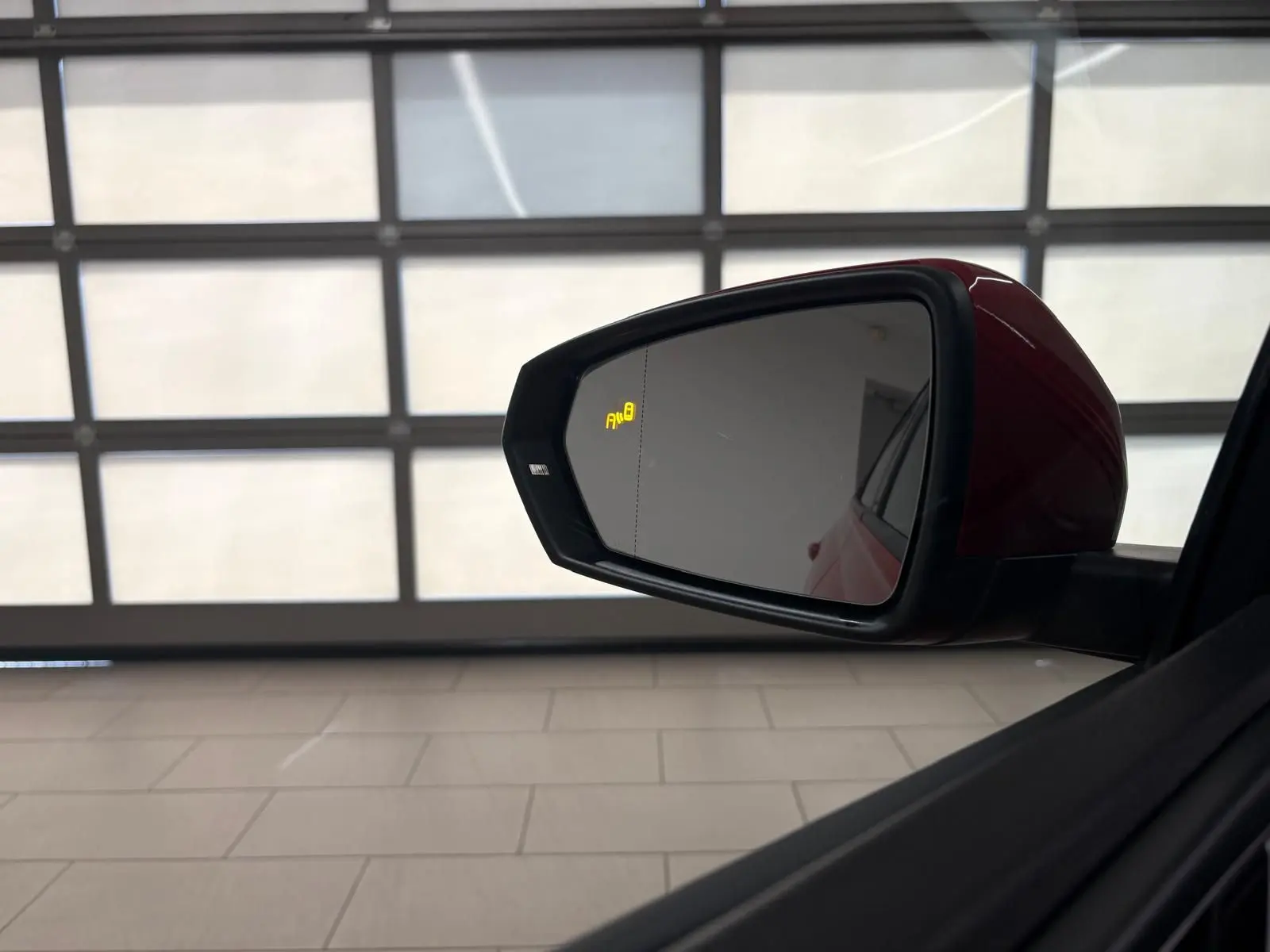 Rétroviseur extérieur côté gauche rouge métallisé de la Volkswagen Polo 1.0 TSI R-Line avec alerte angle mort allumée.