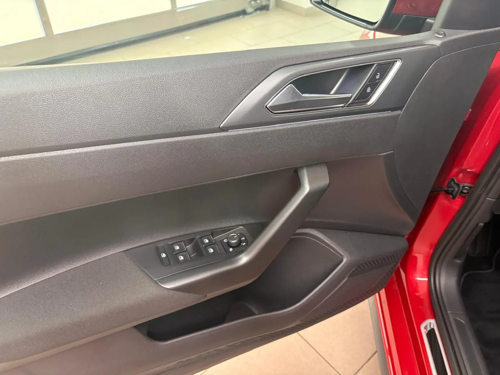 Vue intérieure sur la porte avant gauche rouge Roi d'une Volkswagen Polo 2025 avec commandes de vitres et verrouillage.