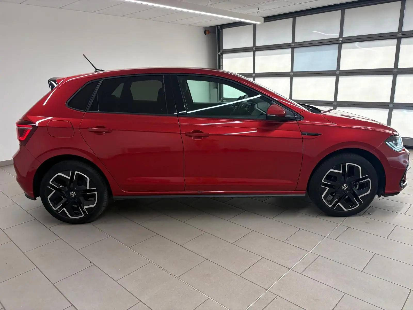 Profil droit d'une Volkswagen Polo 1.0 TSI 95 R-Line rouge métallisé, avec jantes noires et détails sportifs visibles.
