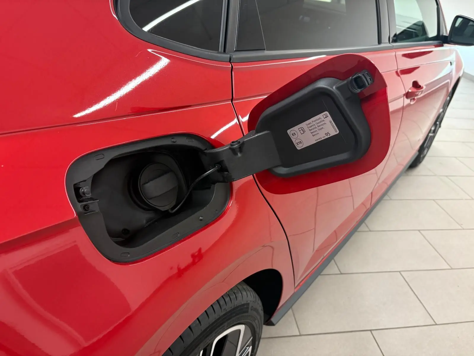 Vue côté gauche arrière d'une Volkswagen Polo Rouge Roi avec trappe de carburant essence ouverte, peinture métallisée brillante.
