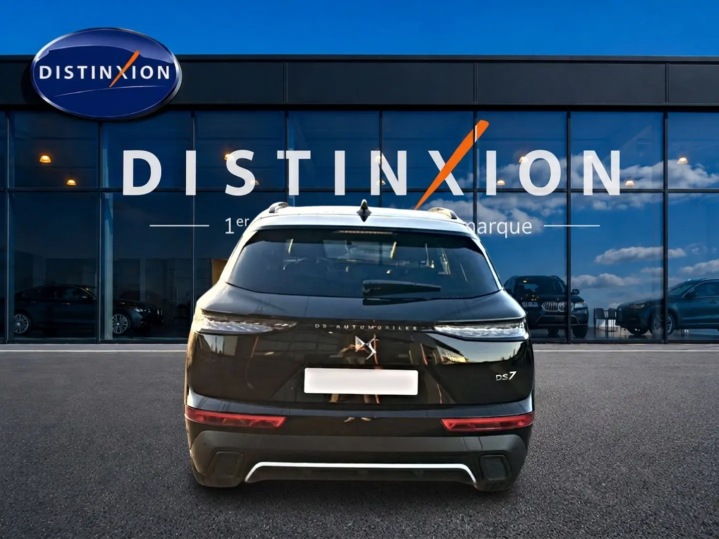 Vue arrière d’un DS7 noir 2026 garé devant une vitrine avec logo Distinxion visible en reflet.