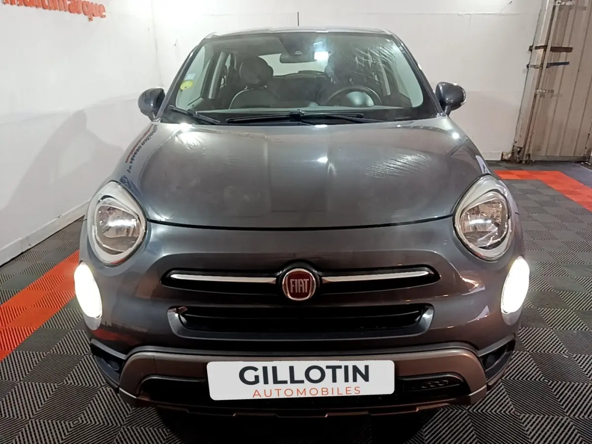 Vue frontale d'une FIAT 500X gris foncé avec phares allumés dans un garage intérieur.