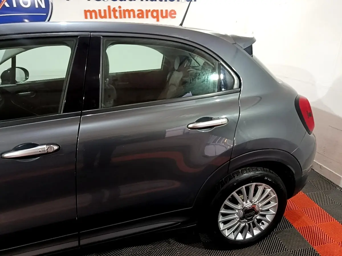 Vue latérale côté droit sur la partie arrière d'une FIAT 500X gris foncé avec jante alliage et poignées chromées.