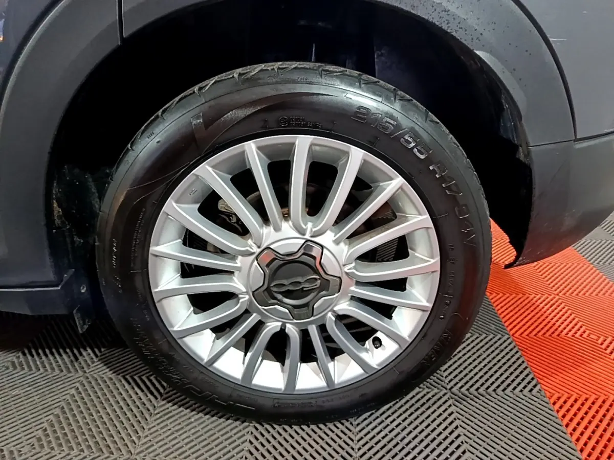 Gros plan sur la roue avant droite d’un FIAT 500X gris foncé, mettant en valeur la jante alliage argentée au design étoilé.