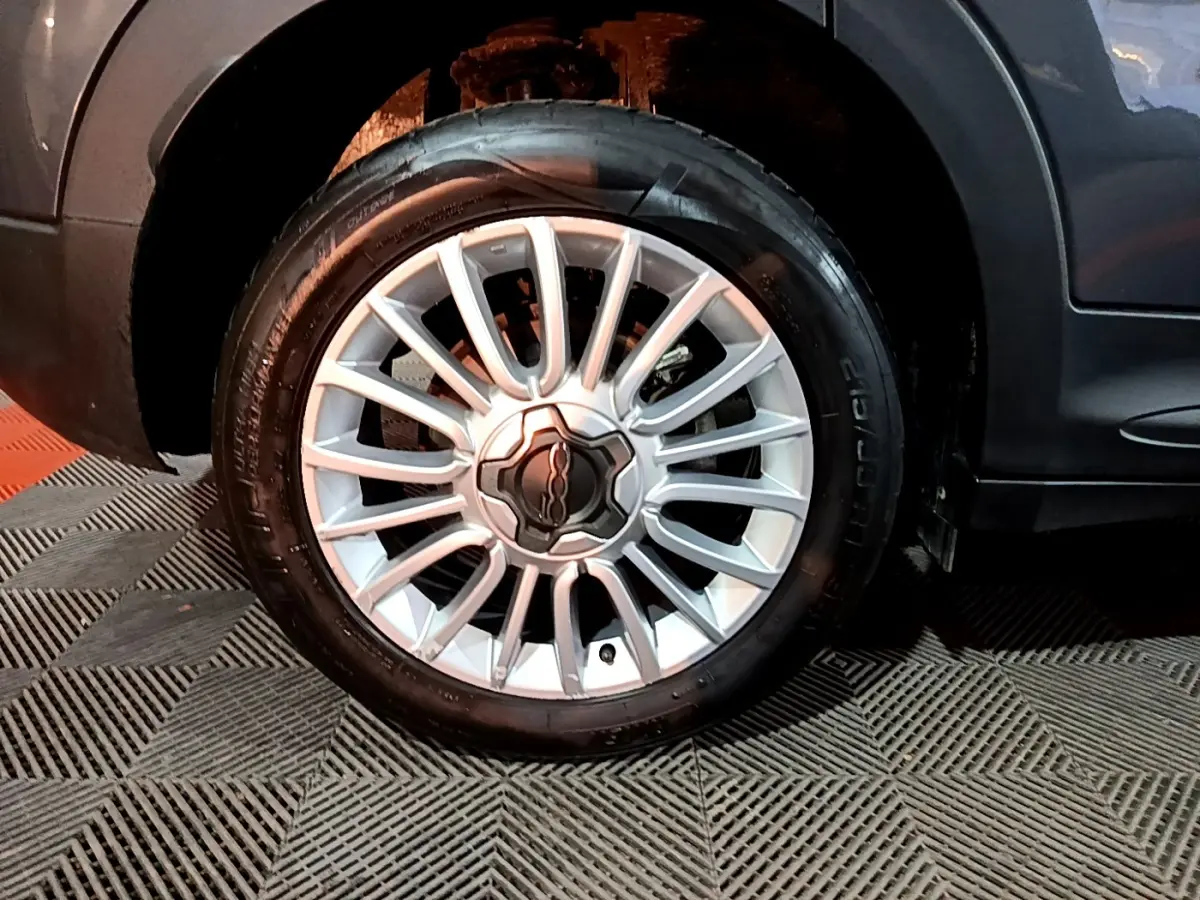 Gros plan sur la roue avant droite avec jante argentée du FIAT 500X gris foncé, partie basse de la carrosserie visible.