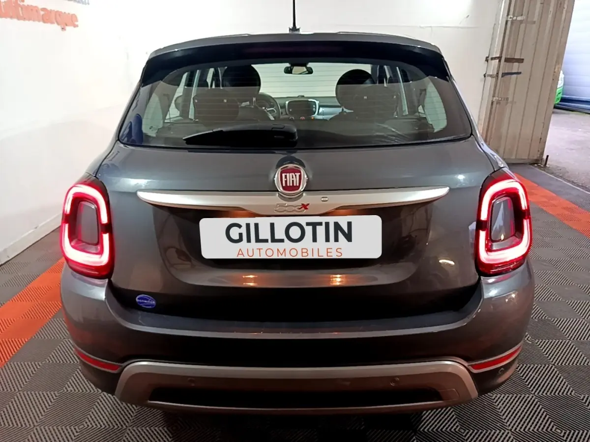 Vue arrière d'une FIAT 500X gris foncé avec feux arrière allumés et logo FIAT visible sur le hayon.