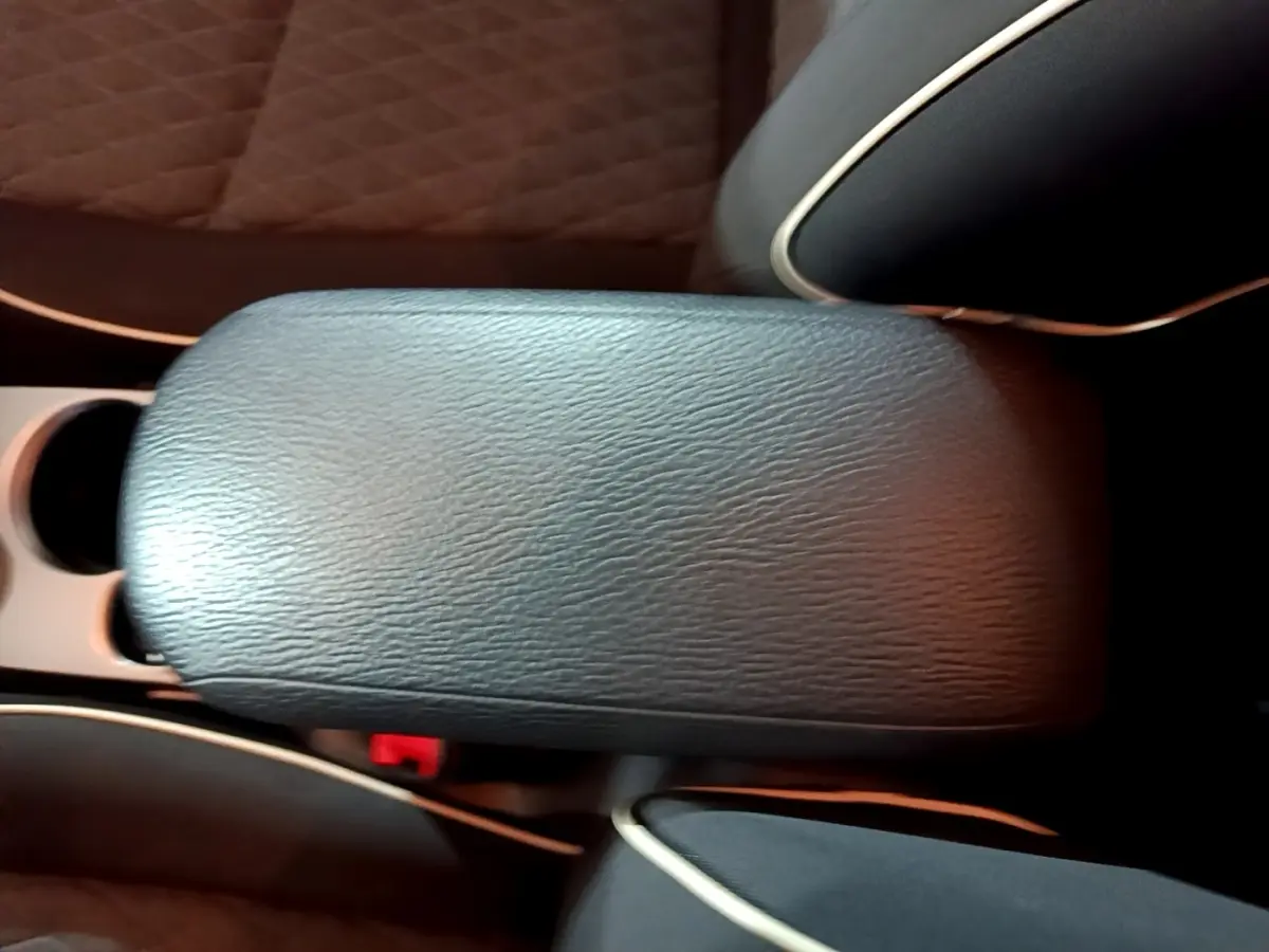 Détail de l'accoudoir central en cuir noir avec surpiqûres blanches dans l'habitacle d'une Fiat 500X gris foncé.