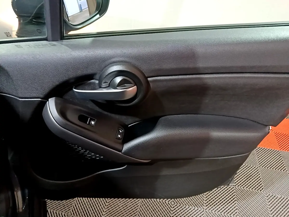 Vue rapprochée de la porte côté conducteur d'une FIAT 500X gris foncé, avec poignée argentée et commandes de vitres.