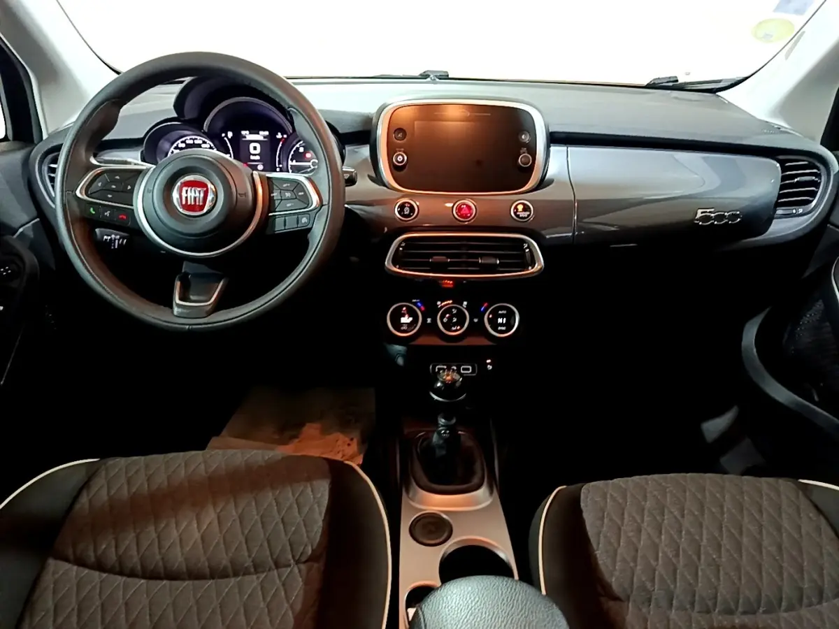 Vue intérieure avant du tableau de bord gris brillant et volant noir de la Fiat 500X avec écran tactile et sièges tissu gris.
