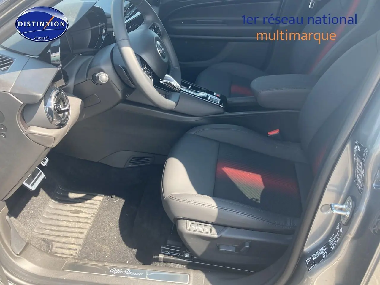 Vue intérieure côté conducteur de l'Alfa Romeo Junior 1.2 hybride gris t/noir, sièges en cuir noir avec surpiqûres rouges.