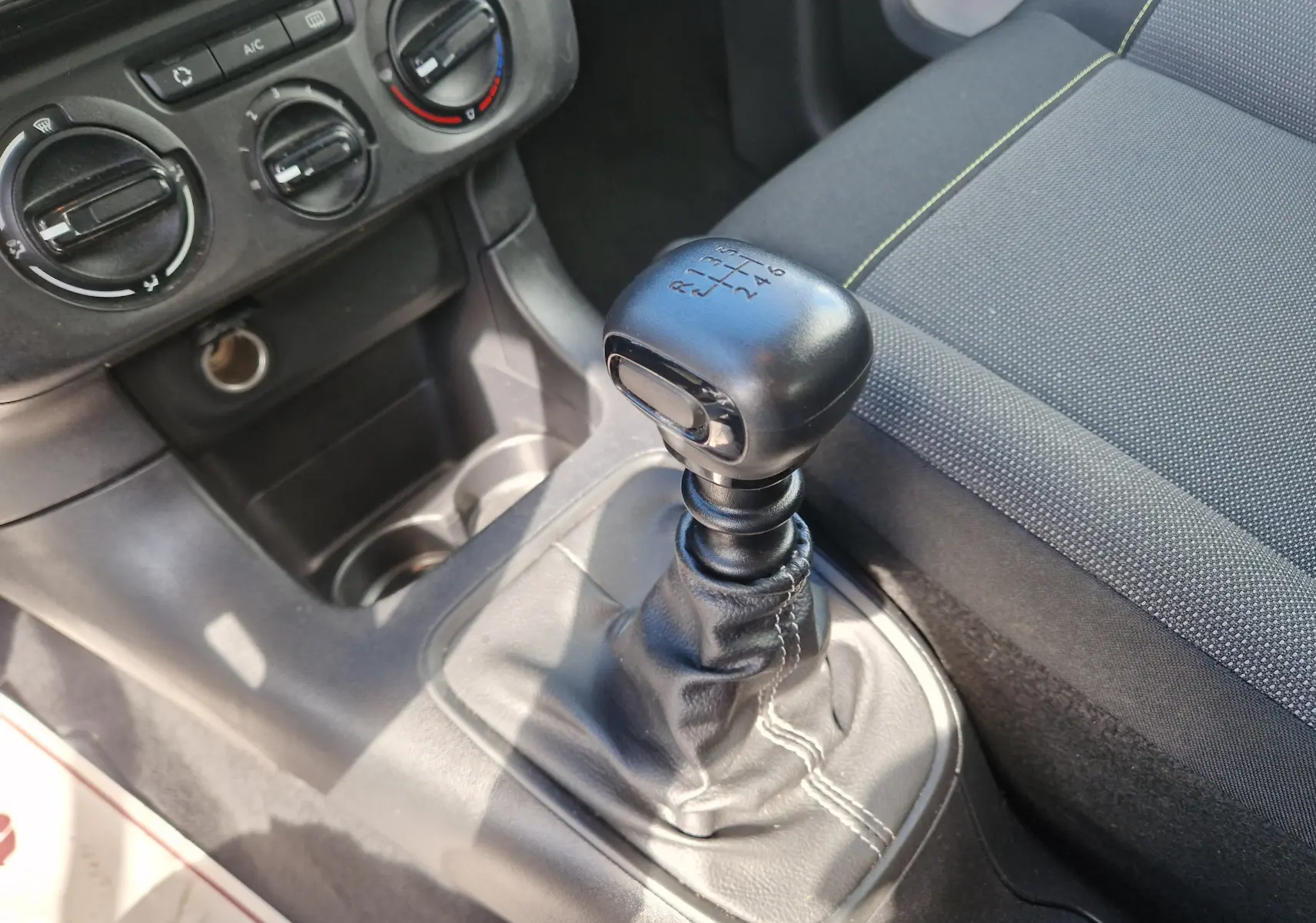 Gros plan sur le levier de vitesses manuel noir et la console centrale du Citroën C3 Société blanc, avec siège tissu gris à coutures claires.