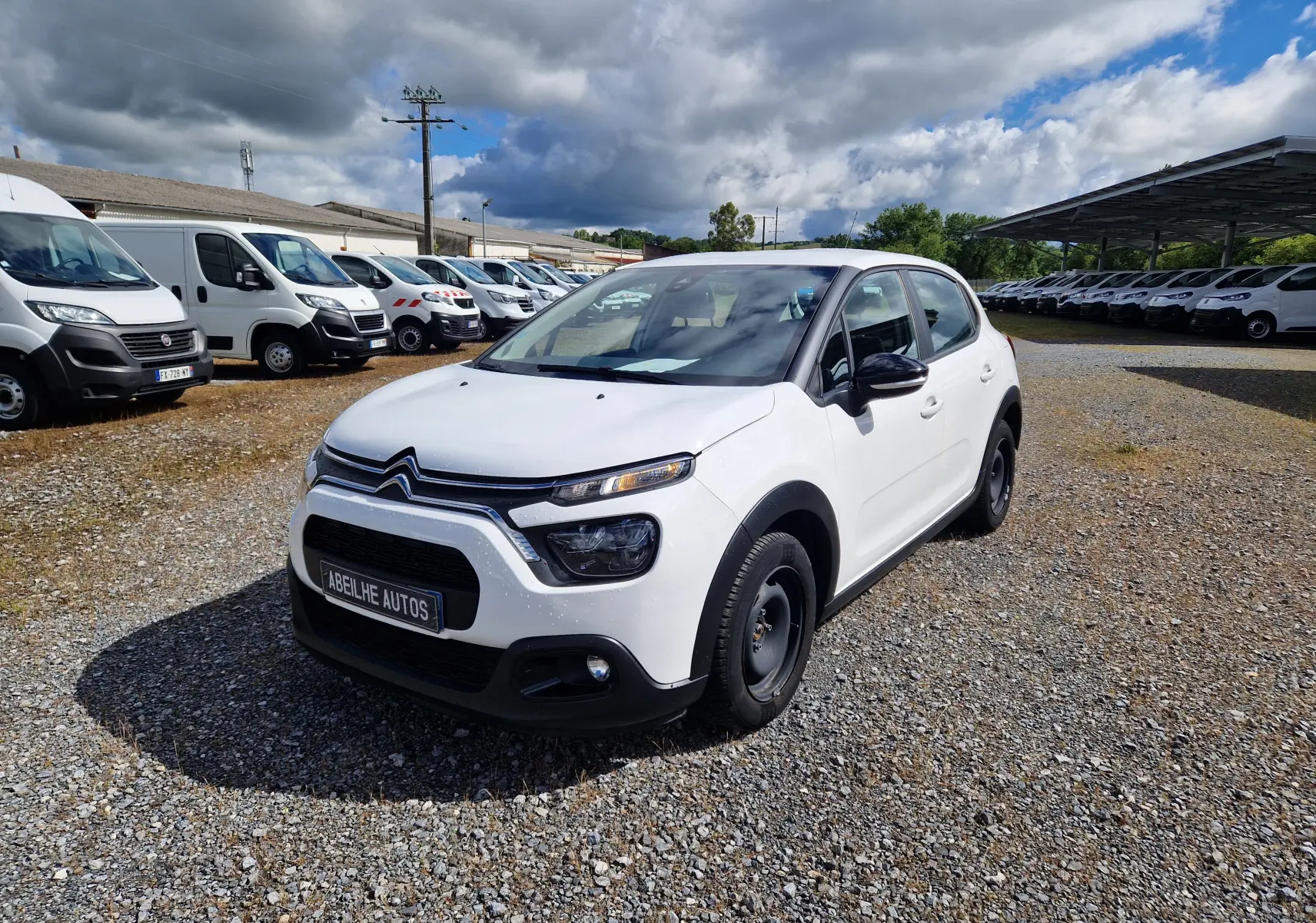 Citroën C3 Société blanche vue en 3/4 avant droit sur un parking avec plusieurs utilitaires en arrière-plan.
