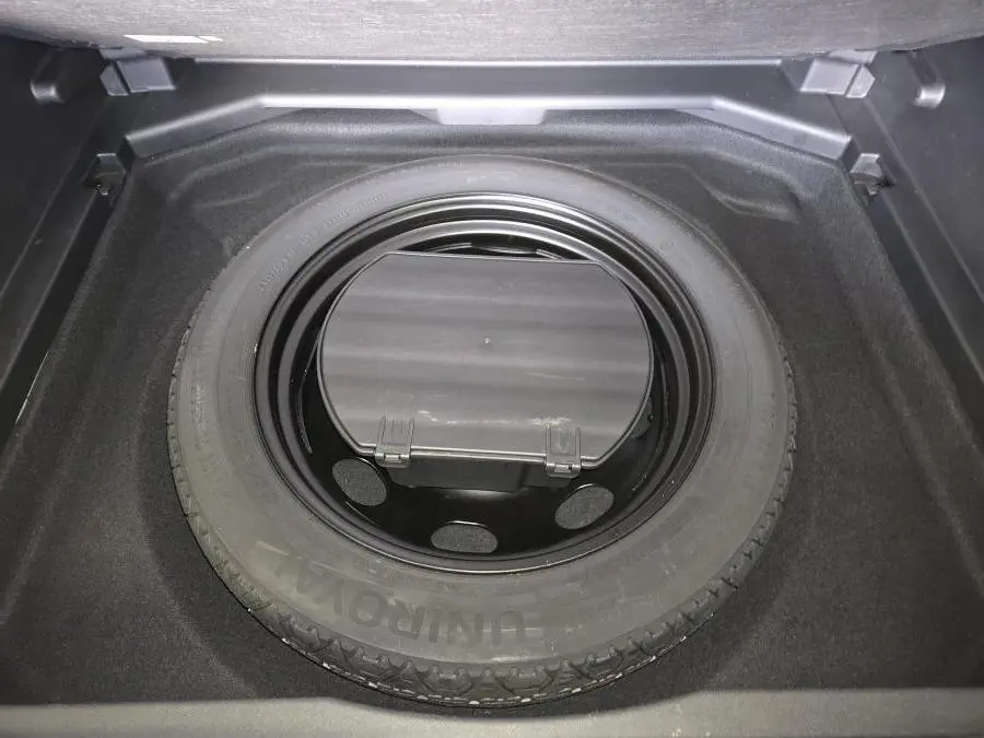 Roue de secours galette noire dans le coffre d’un Peugeot 3008 gris, vue plongeante centrée.