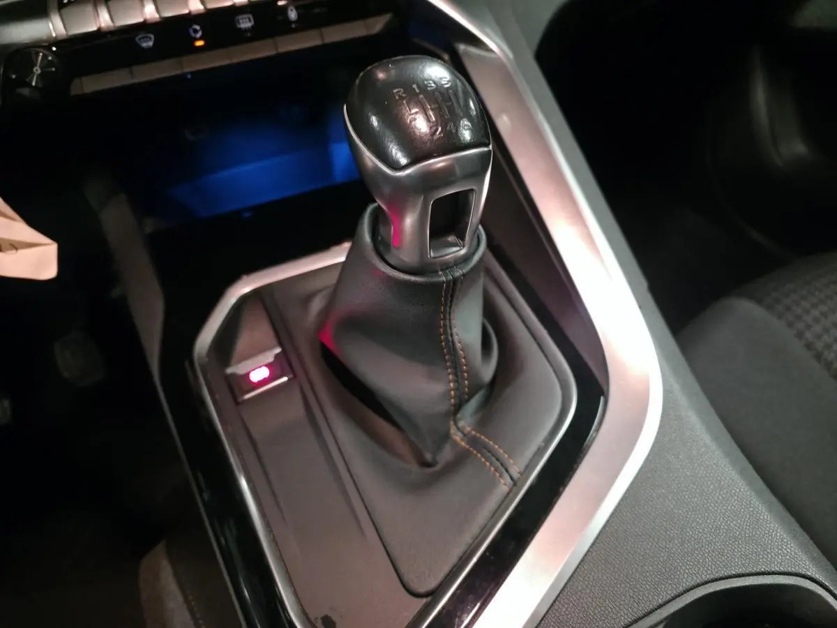 Gros plan sur le levier de vitesses manuel noir avec surpiqûres marron dans le Peugeot 3008 gris.