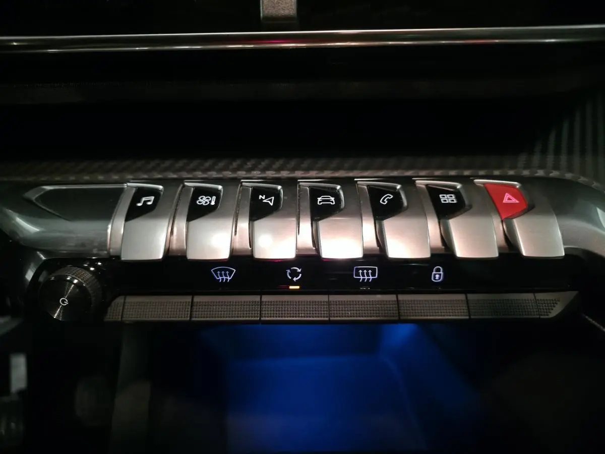 Gros plan sur les commandes chromées et boutons tactiles du tableau de bord du Peugeot 3008 gris, éclairage bleu dessous.