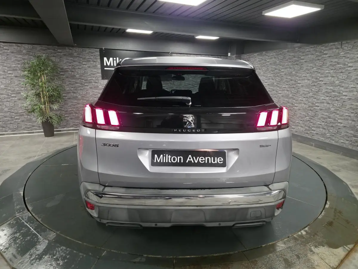Vue arrière d'un Peugeot 3008 gris métallisé avec feux arrière allumés et bandeau noir brillant sur le hayon.