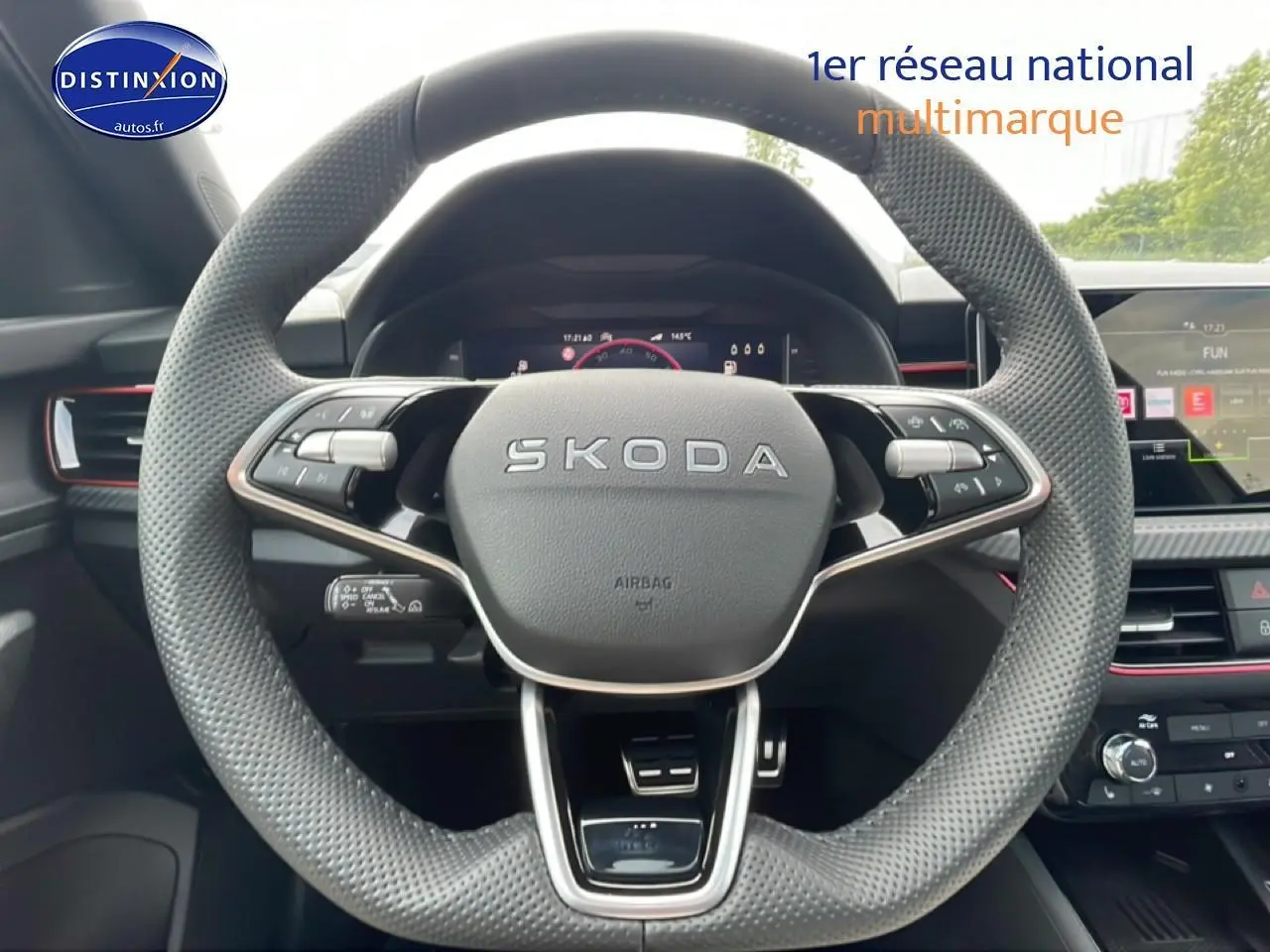 Vue rapprochée du volant cuir perforé SKODA avec commandes multifonctions et tableau de bord numérique en arrière-plan.