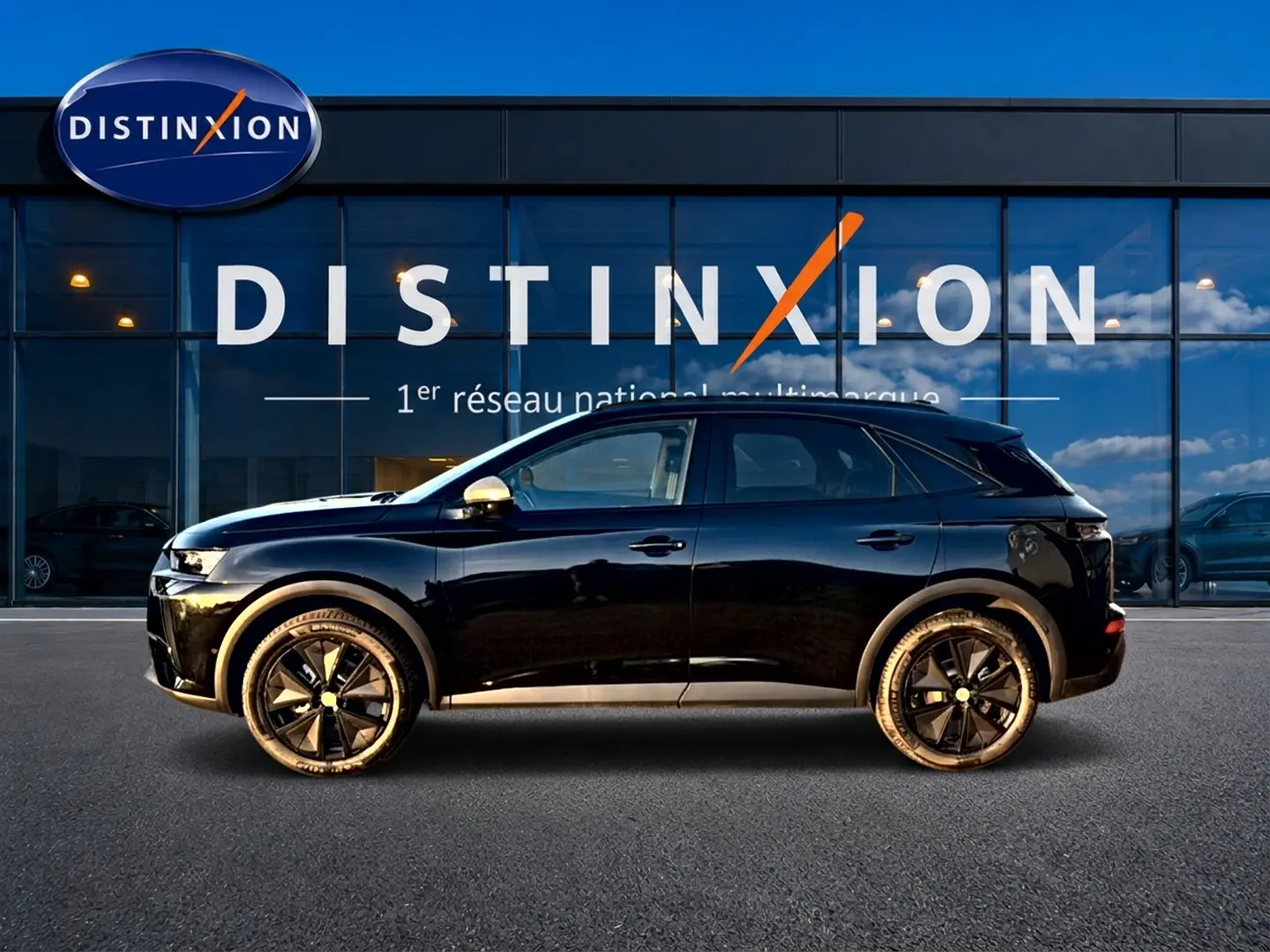 Vue latérale droite d’un DS7 noir brillant avec jantes noires, garé devant une vitrine Distinxion.
