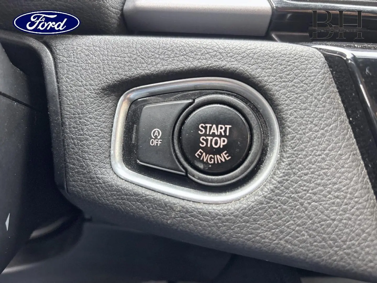 Bouton start-stop moteur en gros plan sur tableau de bord noir texturé, entouré d’un cadre argenté.