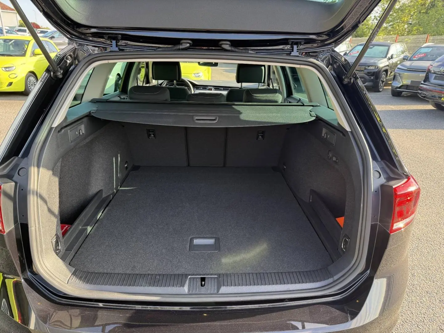 Coffre ouvert vu de l'arrière d'une Volkswagen Passat SW noire intense nacrée, espace de chargement vide et tapis gris.
