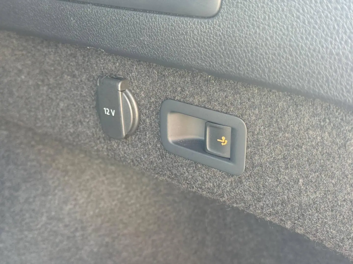 Détail intérieur du coffre de la Volkswagen Passat SW noir nacré montrant prise 12V et bouton rabattage siège arrière.