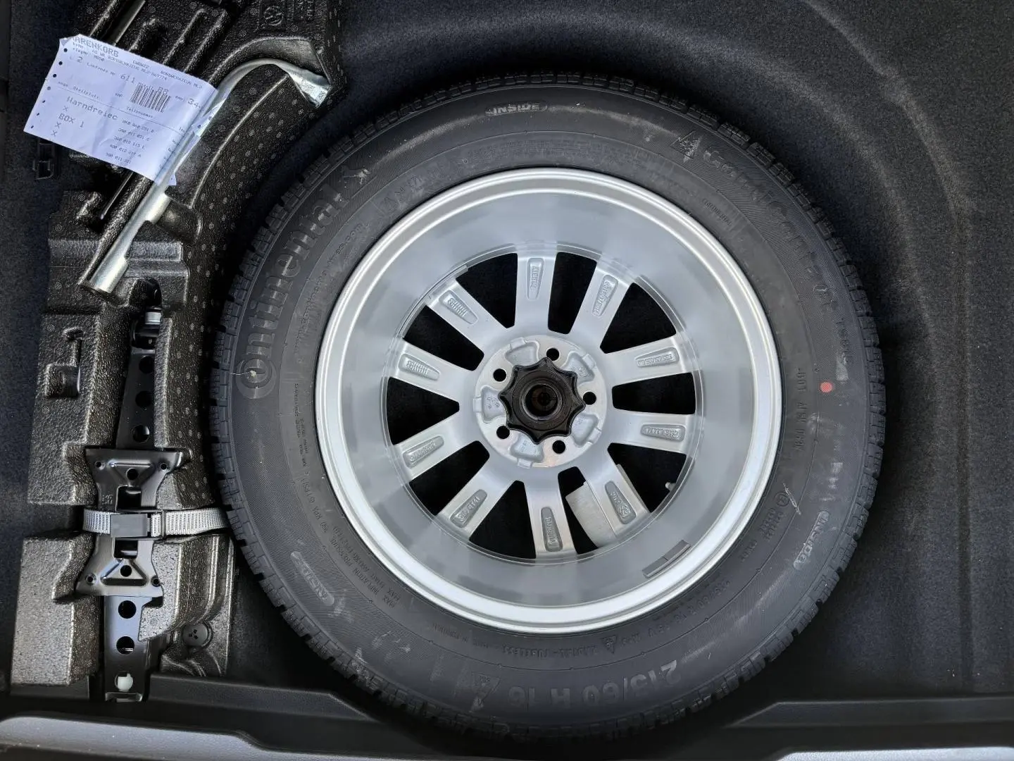 Gros plan sur la roue de secours avec jante acier et cric dans le coffre d’une Volkswagen Passat SW noire.